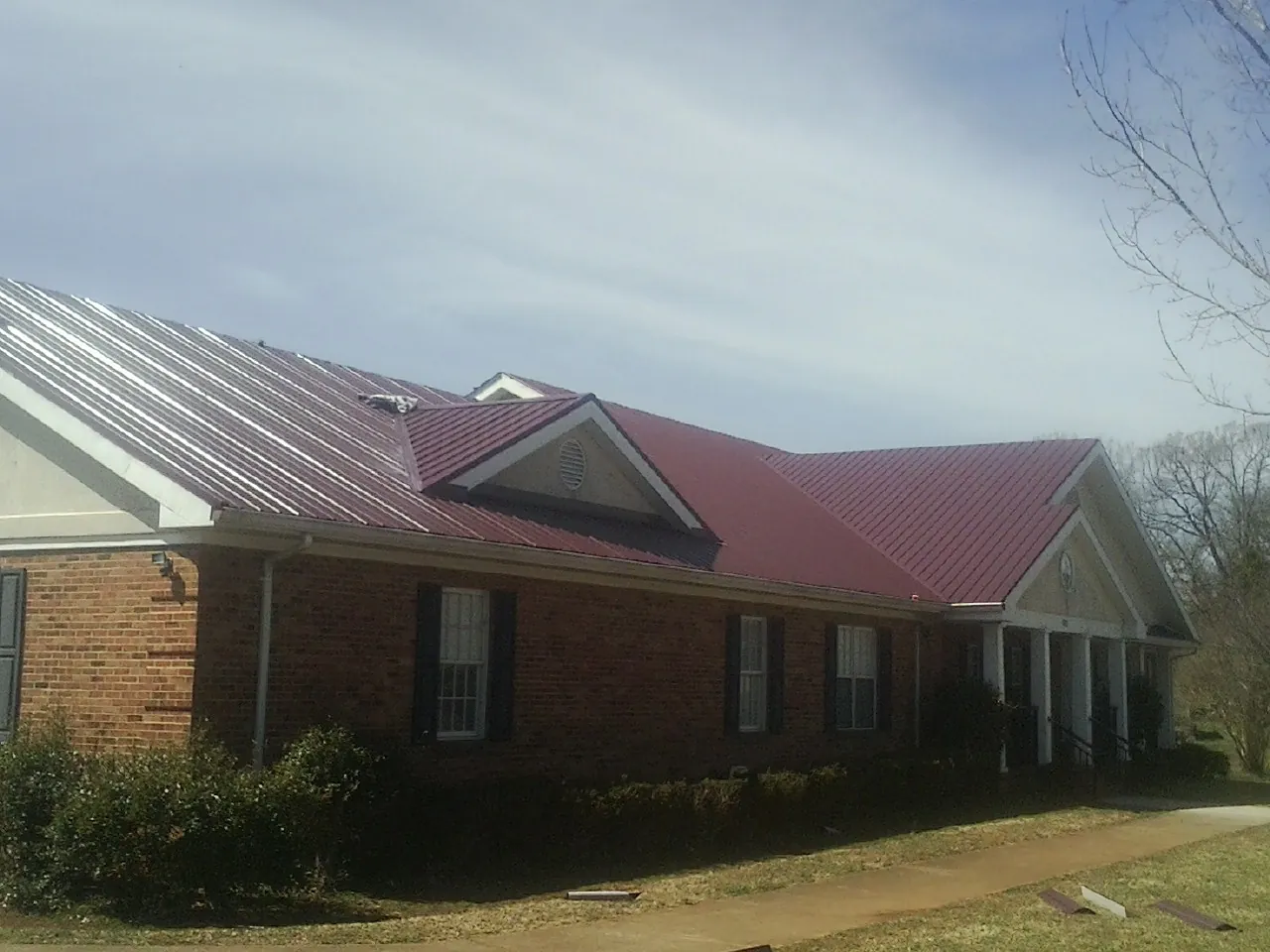 Red metal roof with gabled entries on a long brick building, from a Hail Damage Roof Repair job in Mongaup Valley