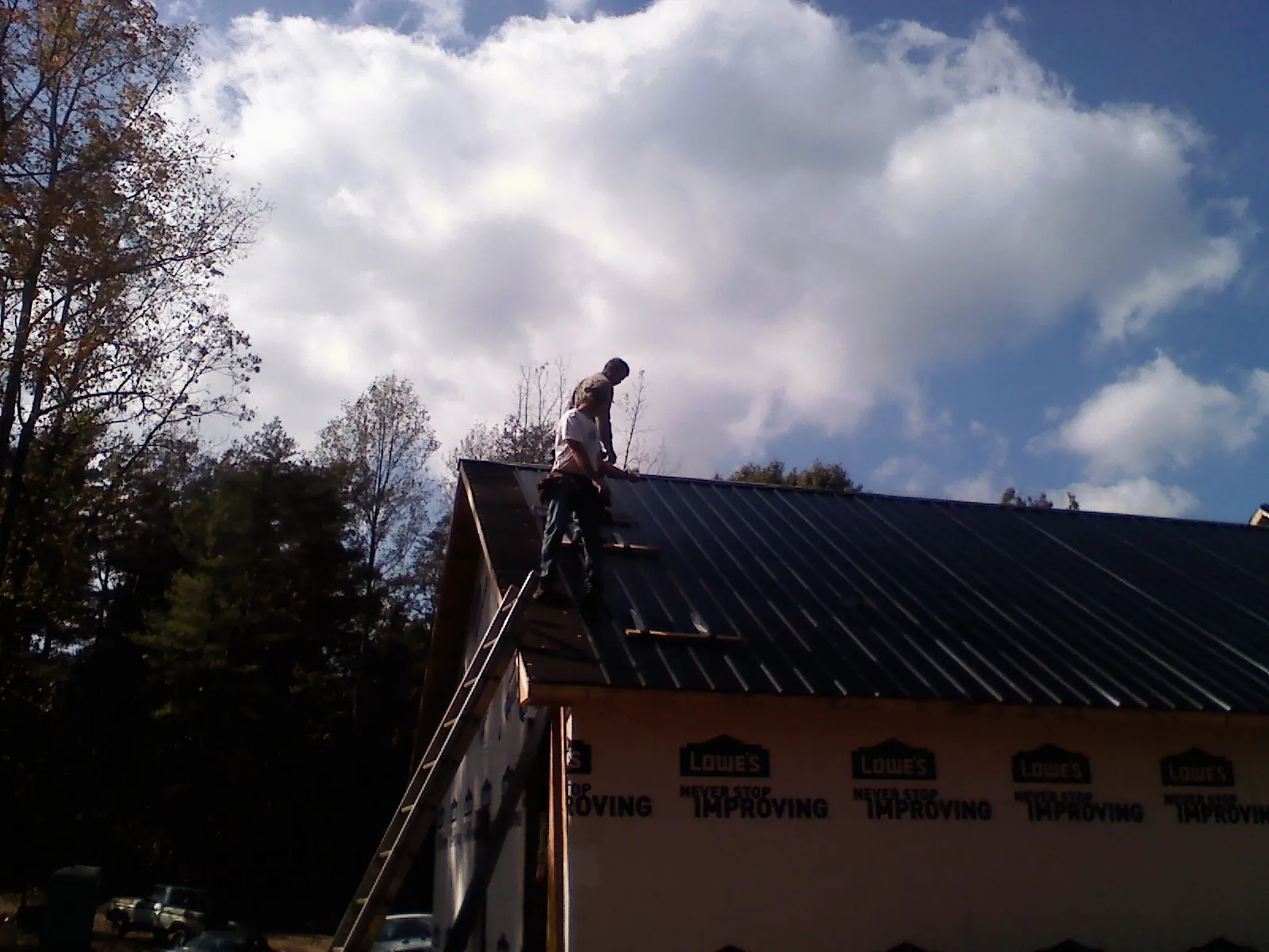 Roofer fastening dark metal panels high against a cloudy sky, from a Roof Inspection job in Mongaup Valley