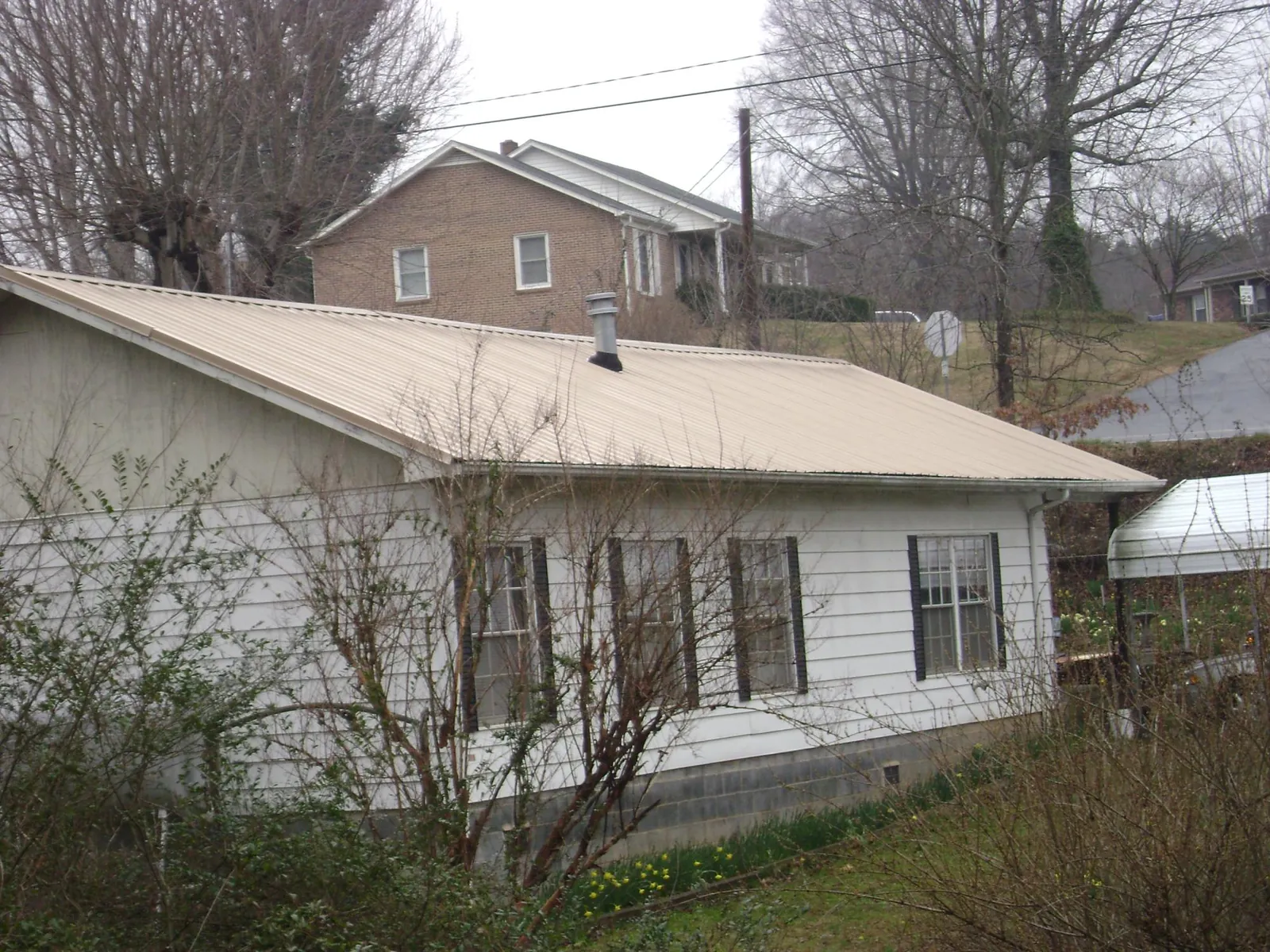 Tan metal roof on a white sided house set into a hillside — Commercial Roofing by Roofing Brothers in Mongaup Valley